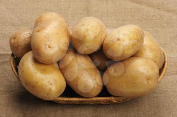 Several brown potatoes in a basket on a sacking