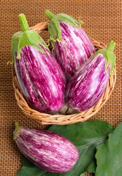 Striped eggplants in a basket on mat