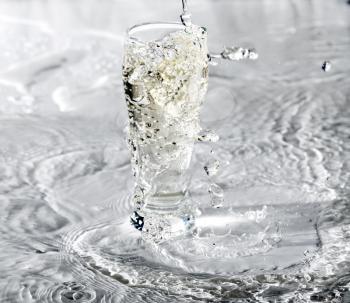 Yelllow drink being poured in a transparent glass with splashes on white