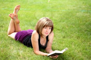 Young happy woman looking at the camera while reading a book in the countryside