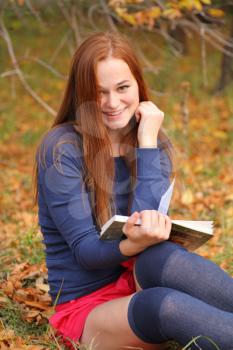 Young beautiful girl with red hair reading a book outdoor in autumn park
