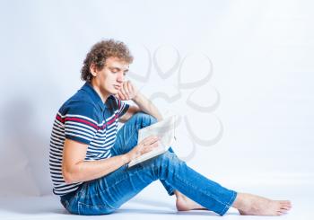 Handsome young student reading a book. Sitting on the gray background. Curly hair.