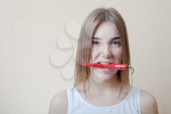 pretty blond woman head and shoulders shot holding in mouth red spicy pepper on beige background. Healthy nutrition diet concept