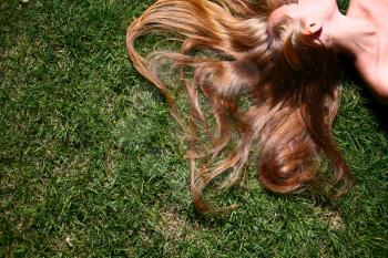 Young woman (no face) with long blond hair lying on the grass sleeping or thinking.