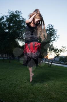 Long haired and free. Young women make jump outdoors at evening. Vertical shot.