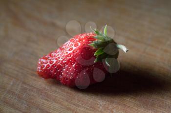 one strawberry on the wooden plank, side view vith long shadow