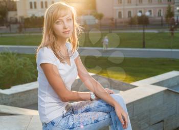 blond against sun sitting on parapet in park and looking at camera
