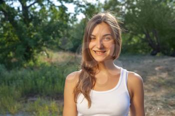 Cute female smiling. Head and shoulders outdoor shot in white tank-top