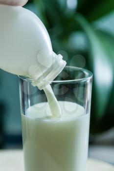 White bottle and milk poured in glass cup over indoors background