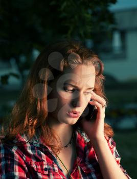 Redhead girl calling by mobile phone outdoors serious face. Toned image.