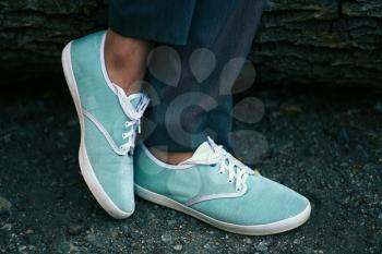 Azure sneakers on womens feet in park closeup.