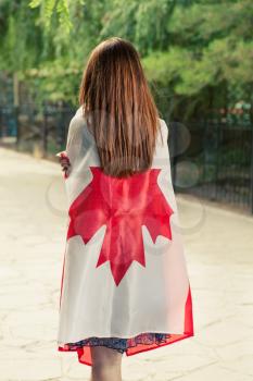 Backside view of young women wrapped around with Canada nation flag.