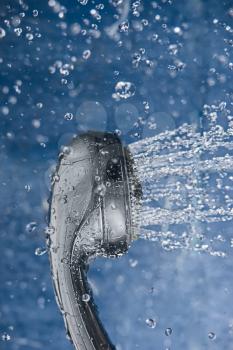 Shower with water stream, on the blue background with water drops levitating around. Flowing water from the shower head and copy space