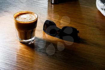 Flat white coffee served on table and sunglasses lay near, copyspace on foreground.