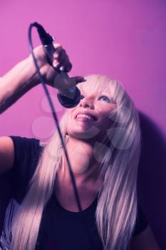 Nice model girl singer with a mic on pink background vertical