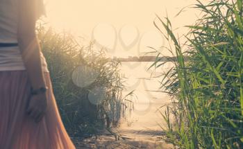 The back view of a young woman in the sunset light on the other side of the river walking towards the water, copyspace.