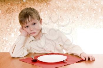 pensive child sits near an empty plate and  looks ahead