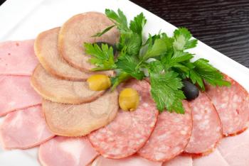 Meat assortment of beef tongue, sausage, meat and ham with greens