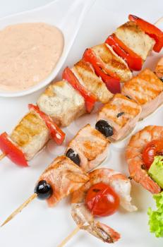 Closeup of grilled shrimps and tomatoes on bamboo sticks with salmon