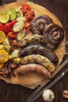 Grilled different meat and fish sausages with vegetables and spices on wooden background