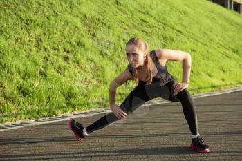 A woman in sportswear doing fitness exercises. City in sunny evening.