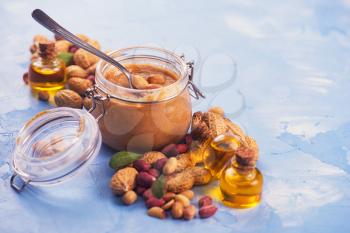 Natural peanut butter with oil in a glass jar and peanuts