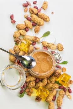 Natural peanut butter with oil in a glass jar and peanuts