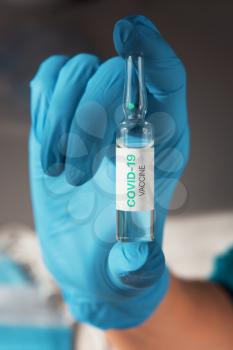 Coronavirus vaccine concept: covid-19 vaccine in hand with blue protective gloves.