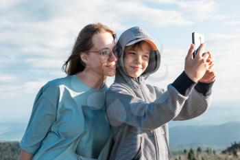 A child takes a selfie on a smartphone with mom in the mountain trip.