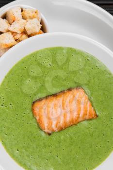 Delicious green broccoli cream-soup with salmon and crackers on white plate
