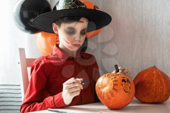 Teen boy in costume drawing coronavirus image on the pumpkin for the Halloween celebration. Halloween carnival with new reality with pandemic concept.