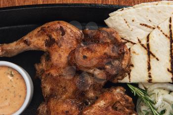 Appetizing grilled juicy chicken with golden brown crust served with barbeque sauce, rosemary and pita bread.