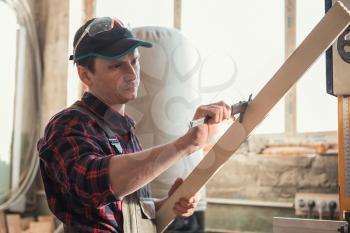 The worker makes measurements of a wooden board with corner ruler.