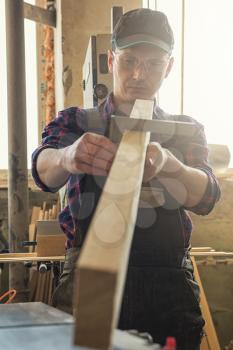 The worker makes measurements of a wooden board with corner ruler.