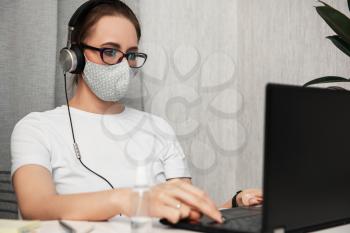 Woman working with notebook. Protective mask and Sanitizer spray on the working place