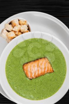 Delicious green spinach cream-soup with salmon with crackers on white plate
