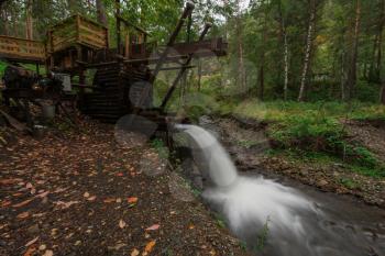 Rustic watermill with wheel being turned by force of falling water from Altai mountain river. Slow shutter speed.