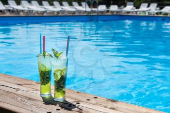 Two Mojito cocktail with lime and mint in highball glass on the swiming pool background. Concept of summer relaxing