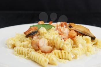 Seafood Pasta with mussels salmon and shrimps with basil in white plate on black wooden background.