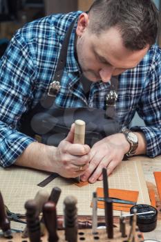 Man working with leather textile at a workshop. Craftman cutting leather. Concept of handmade craft production of leather goods.