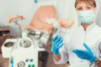 Female gynecologist in protective mask and whitecoat with gynecological vaginal retractor in hand