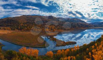 Aerial view of road and lake in beautiful autumn Altai forest. Beautiful landscape with empty rural road, golden autumn in altai: trees with red, yellow and orange leaves.