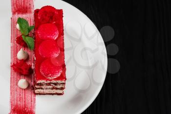 Plate with piece of delicious red velvet cake on black wooden background, food and drink concept