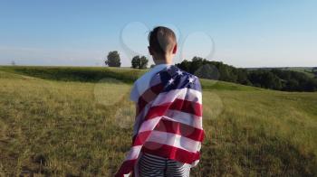 Blonde boy waving national USA flag outdoors over blue sky at the river bank.