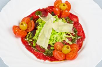 Meat carpaccio from beef meat, parmesan cheese, olive, tomato, sauce pesto