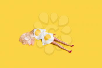 Concept for sunbathe. Doll with fried eggs on yellow background