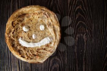 Fried smiling pancakes with sour cream on old wooden table