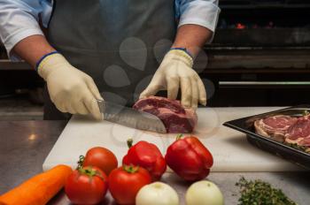 Chef cutting meat on steaks with knife