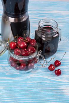 Cherry juice with glass jar,of berries, blender and juice on blue wooden background