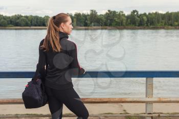 A woman in sportswear with bottle of water on embankment background